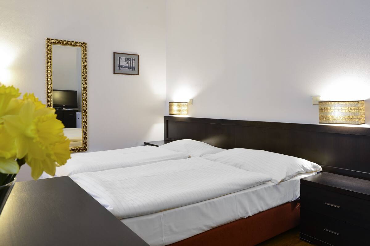 A hotel room with a large bed, a nightstand, a mirror, and a wall-mounted light fixture.