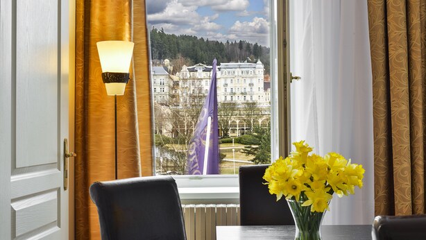 Een hotelkamer met uitzicht op een gebouw, een tafel met een bloevas en een lamp.