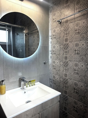 A bathroom with a white sink, a round mirror, and patterned tiles. - Irene Studios (Istiaia-Aidipsos)