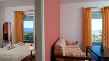 Quarto de hotel com duas camas, um sofá, uma mesa e varanda com cortinas laranja.