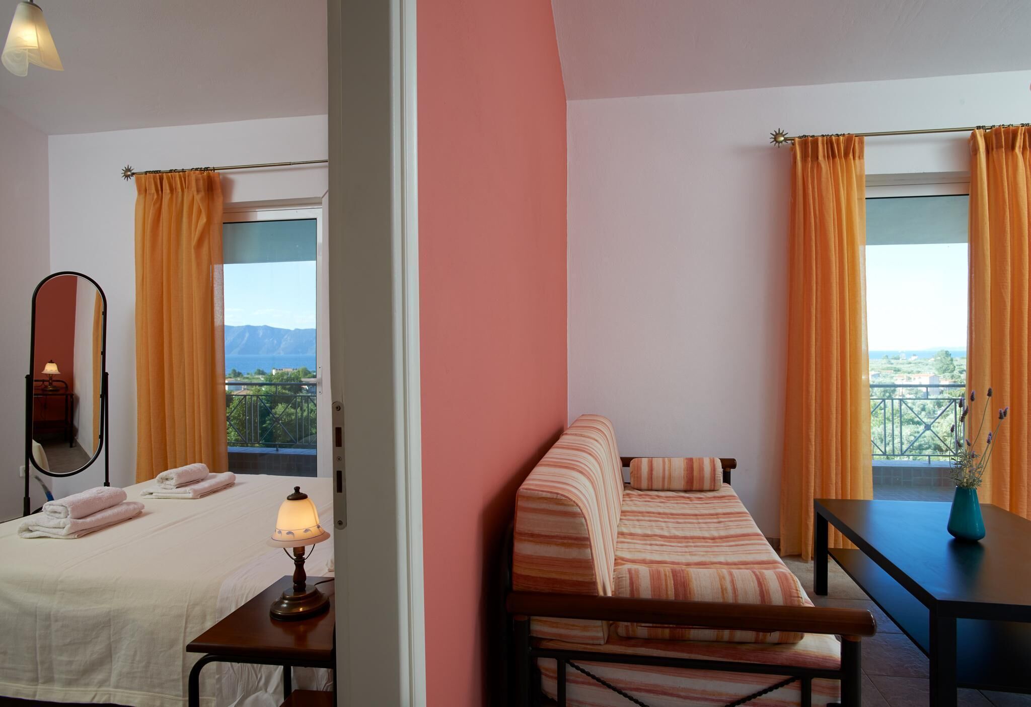 Une chambre d’hôtel avec deux lits, un canapé, une table et un balcon agrémenté de rideaux orange.
