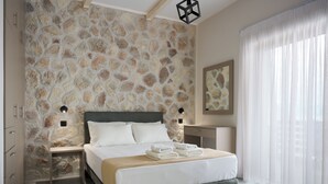 Un dormitorio moderno con pared de piedra, cama con sábanas blancas, mesita de noche con lámpara y ventana grande con cortinas traslúcidas.