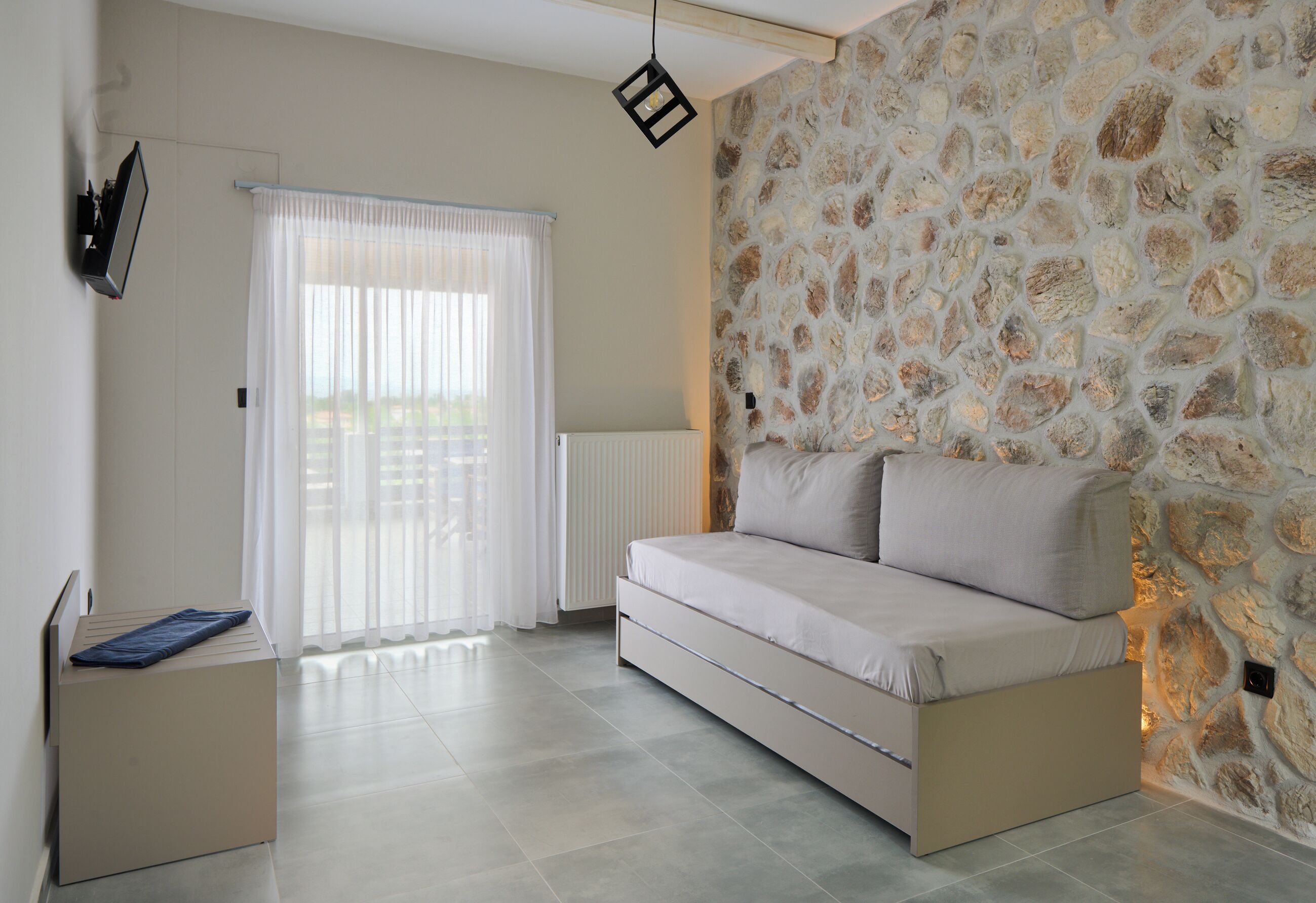 A modern bedroom with a stone wall, a sofa bed, a radiator, and a window with curtains.