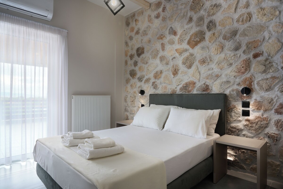 A bedroom with a stone wall, a bed with white linens, and a bedside table with a lamp.
