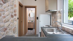 Una cocina moderna con pared de piedra, armarios de madera, un lavamanos de acero inoxidable y ventana con vistas a la vegetación.