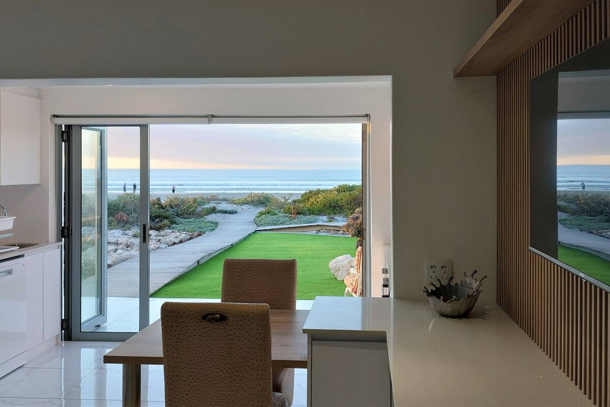 A modern kitchen with a view of a landscaped garden and beach.