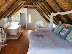 A bedroom with a wooden ceiling, a large bed with patterned bedding, a nightstand, and a bedside table.