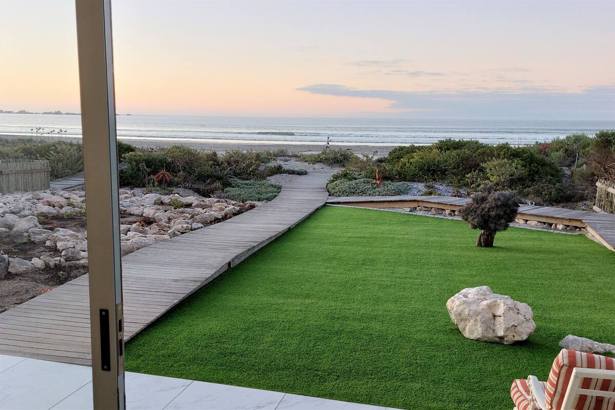 A landscaped garden with a wooden deck, a green lawn, and a view of the ocean.