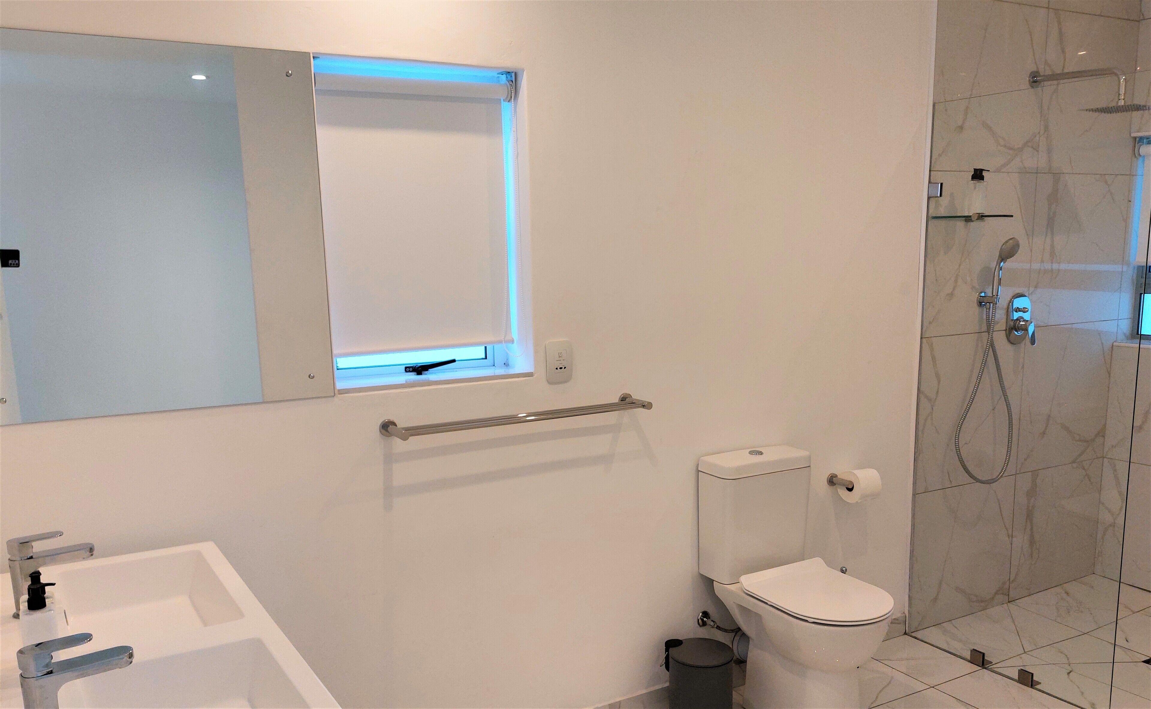 Een moderne badkamer met een wit wastafel, toilet en douche.