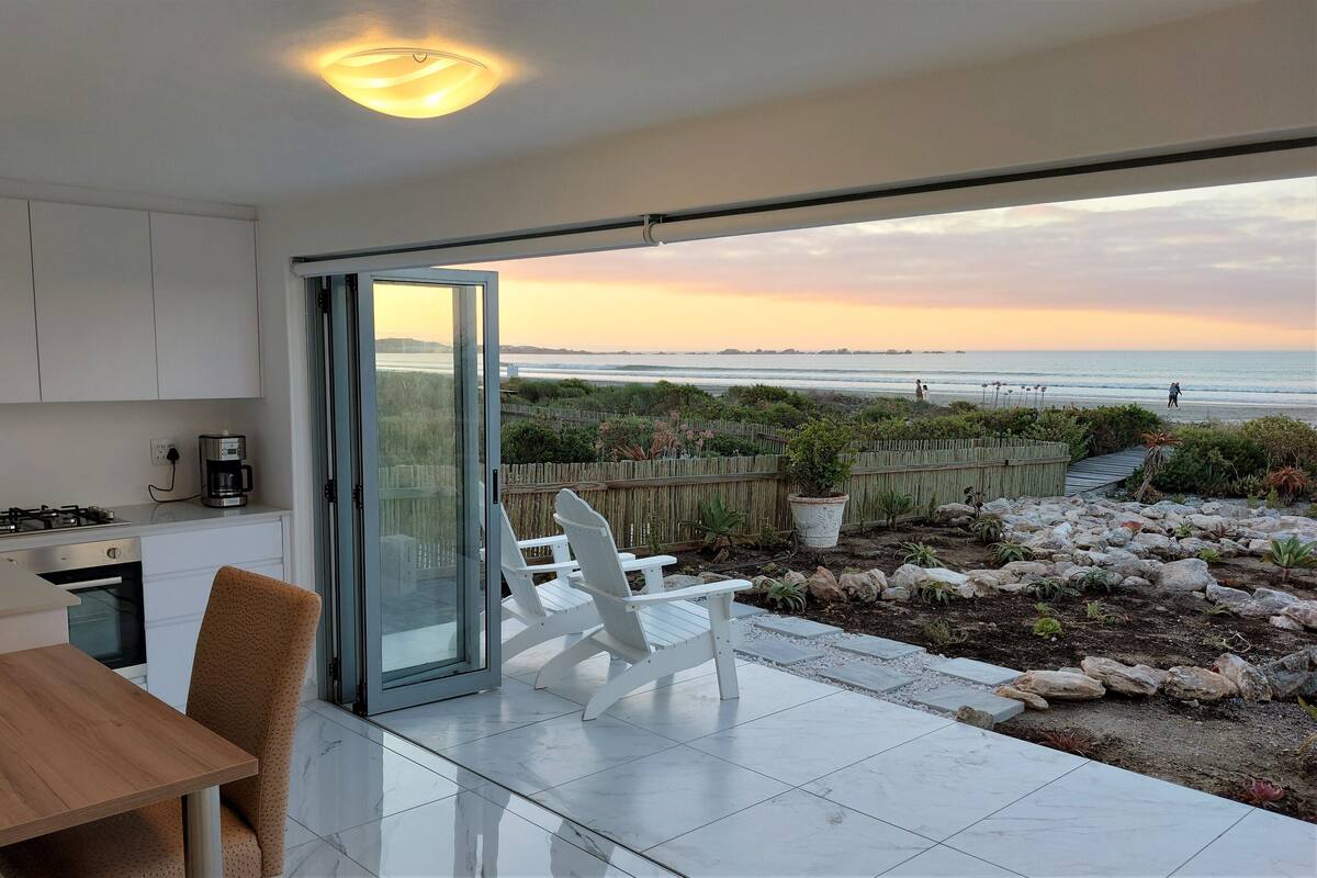 A modern kitchen with a sliding glass door leading to a patio with a view of the beach and ocean.