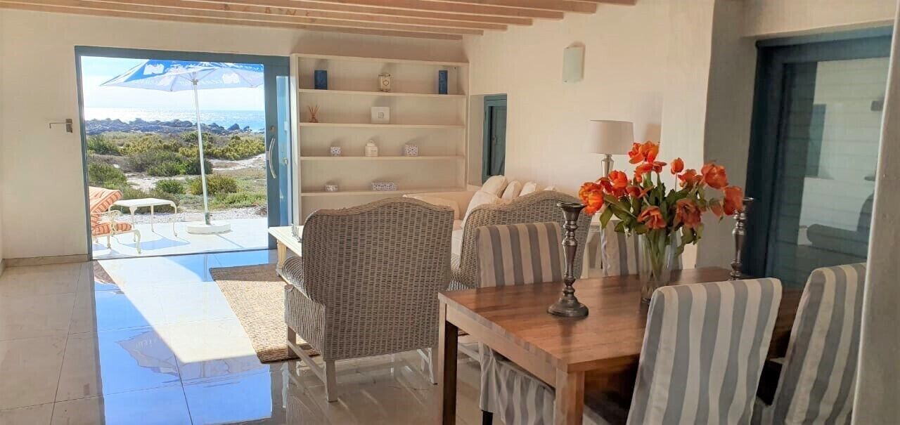 Une pièce comprenant une table à manger, des chaises, un vase avec des fleurs, une bibliothèque et une vue sur l’extérieur.