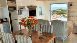 Une cuisine moderne dotée d’appareils électroménagers intégrés, un coin repas avec des chaises à rayures et une vue sur la mer par une porte ouverte.