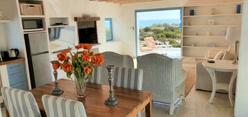 Una cocina moderna con electrodomésticos integrados, un comedor con sillas a rayas y vistas al mar a través de un ventanal.