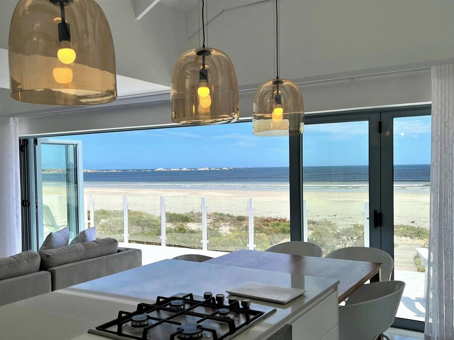 A modern kitchen with a gas stove, a dining area with a large table, and a view of the beach through large windows.