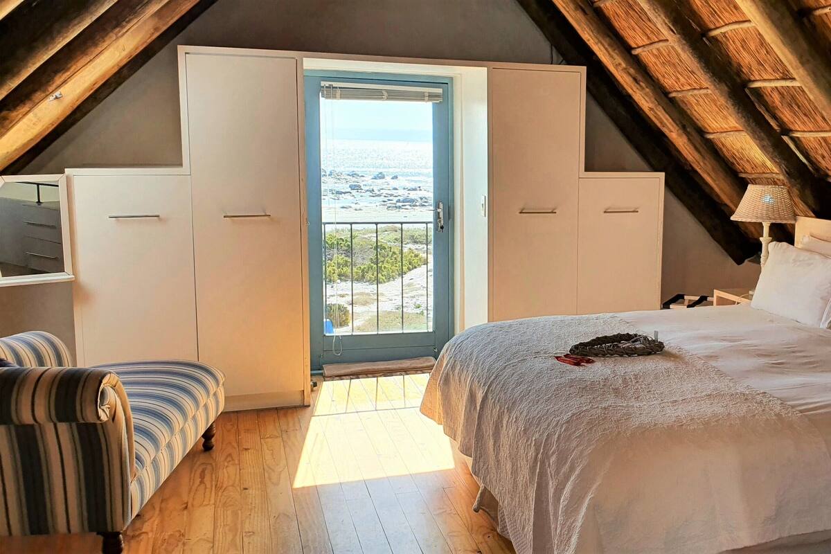 A bedroom with a large bed, a view of the sea through a balcony door, and a wooden ceiling.