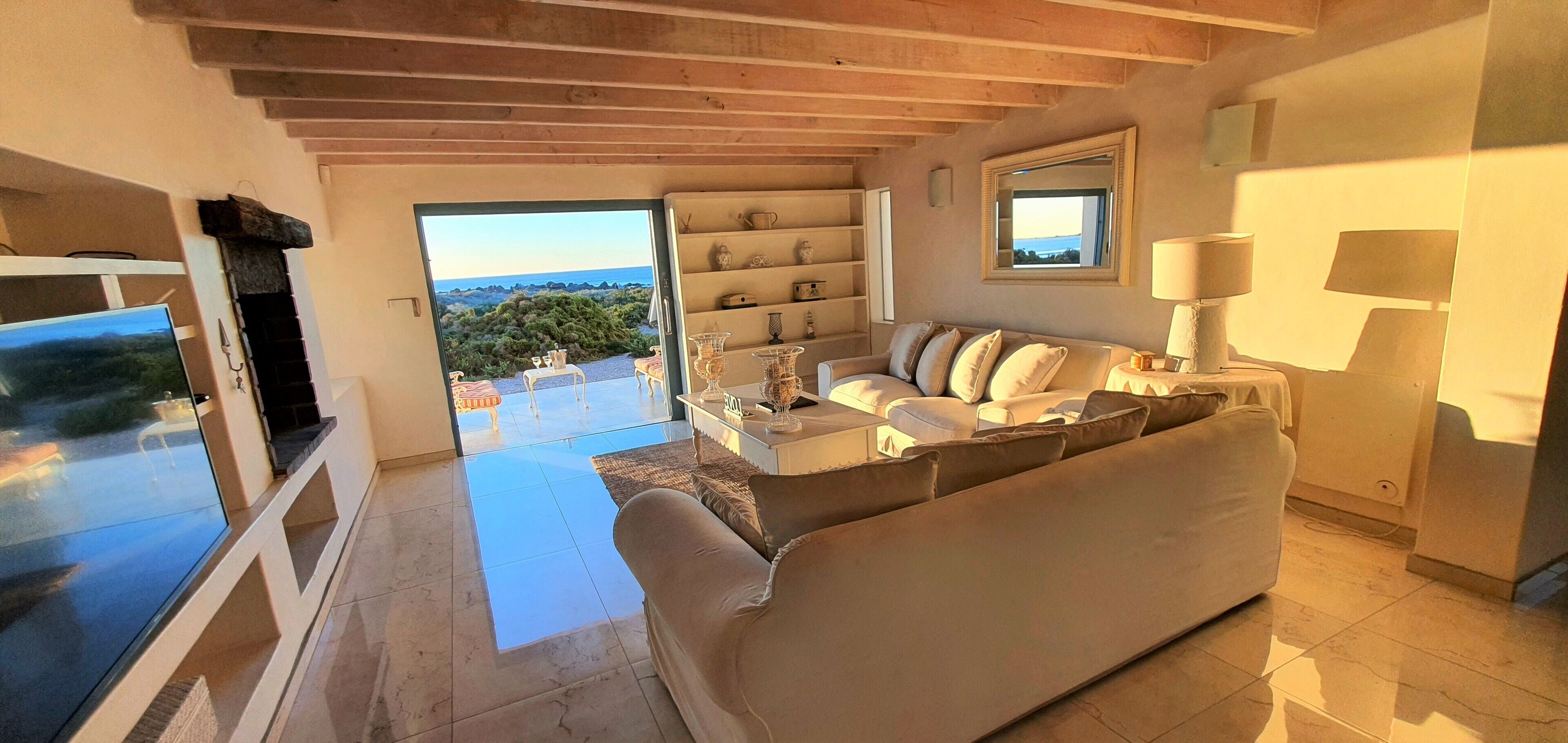 A spacious living area with a sofa, a coffee table, and a TV. There is a view of the outdoors through a glass door.