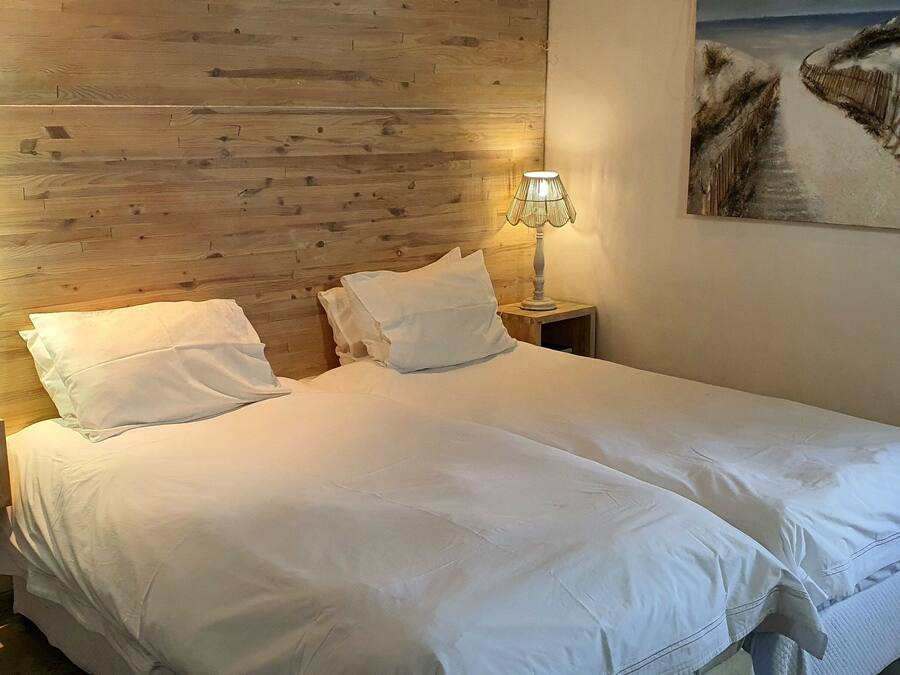 Ein Doppelbett mit weißen Leinentüchern, zwei Nachttische mit Lampen, ein hölzernes Kopfende und ein Gemälde mit Strandmotiv an der Wand.