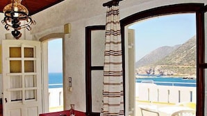 A room with a view of the sea, a red table, and a curtain.