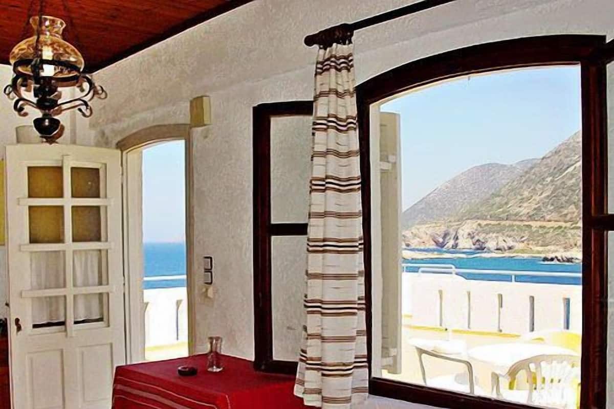 Une pièce avec vue sur la mer, une table rouge et un rideau.