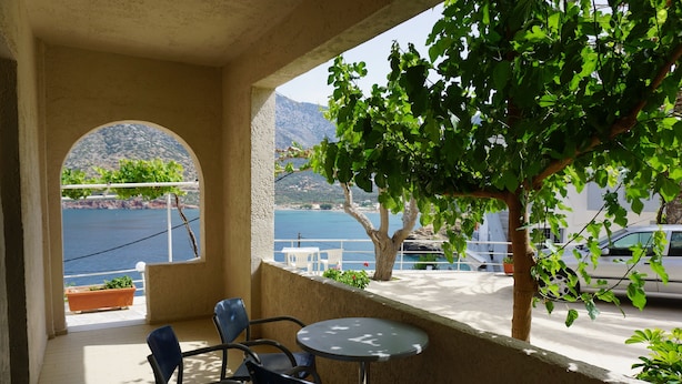 A balcony with a table and chairs, overlooking a body of water and mountains.