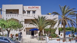 A building named "Valentino" with a white facade, multiple balconies, and a palm tree in the foreground.