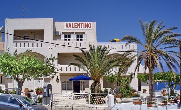 A building named "Valentino" with a white facade, multiple balconies, and a palm tree in the foreground. - Valentino Apartments and Studios (Mylopotamos)