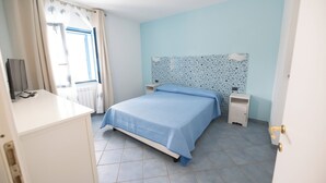 Une chambre à coucher avec un lit, une table de chevet, une commode et une fenêtre avec des rideaux.
