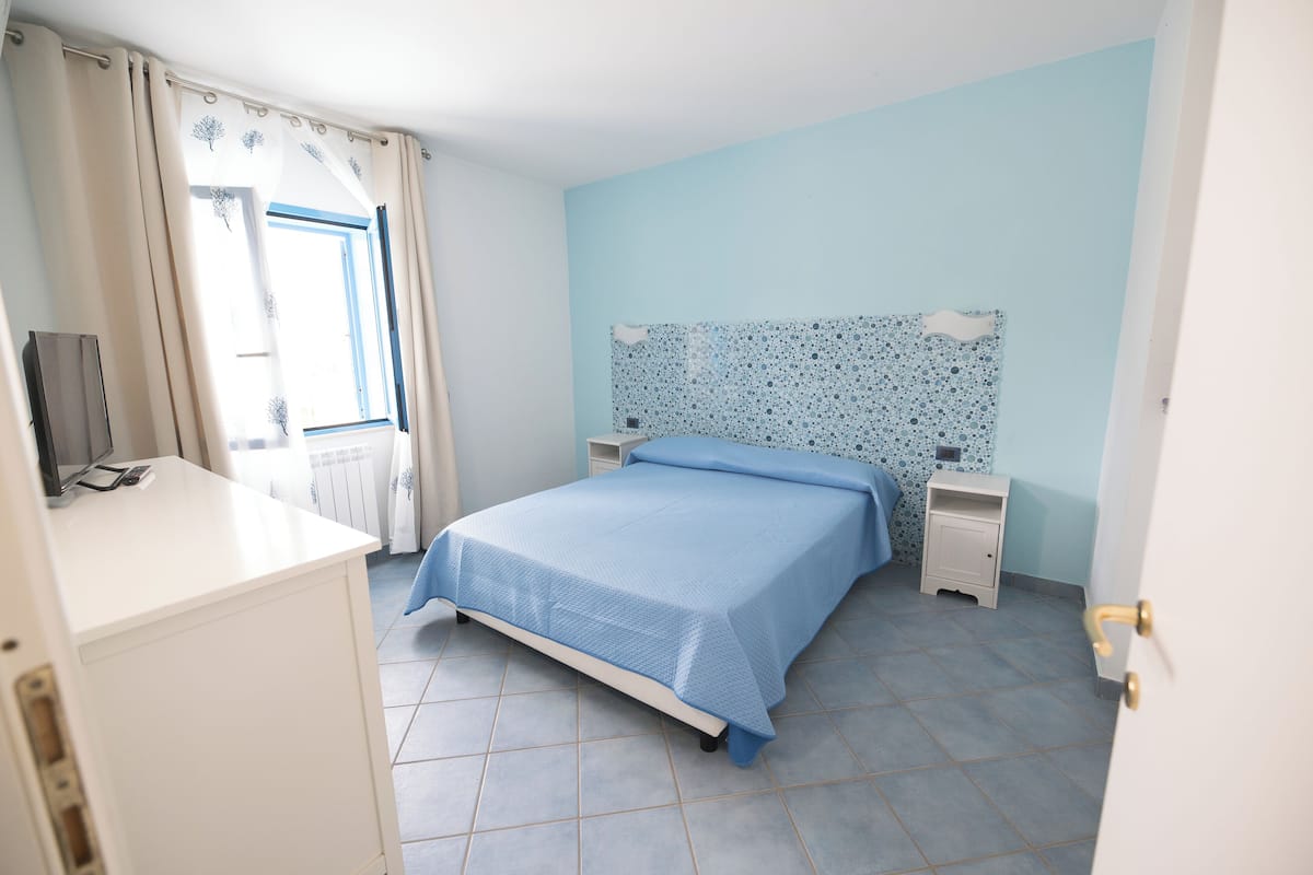 A bedroom with a bed, a nightstand, a dresser, and a window with curtains.