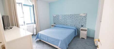 A bedroom with a bed, a nightstand, a dresser, and a window with curtains.