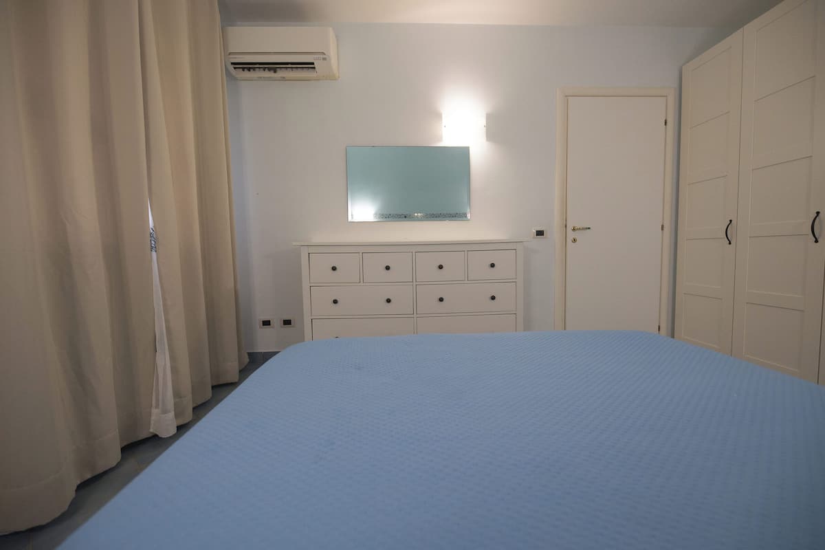 A bedroom with a bed, a dresser, an air conditioning unit, and a door.