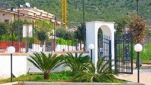 Un quartier résidentiel doté d’une entrée sécurisée, un bâtiment blanc avec un toit rouge et un chemin bordé de lampadaires et de verdure.