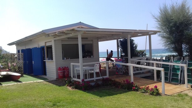 Une petite construction située au bord de la plage, dotée d’un patio couvert, d’une table et de chaises.