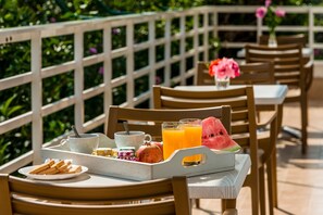 A breakfast tray with toast, a pomegranate, a watermelon slice, and orange juice on a wooden table outdoors.