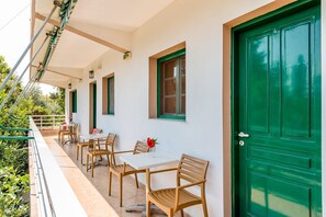 A covered outdoor seating area with tables and chairs, a green door, and a balcony railing.