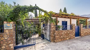 A stone-walled building with a blue door and a metal gate. - Alpha Stegna Sun (Rhodes)
