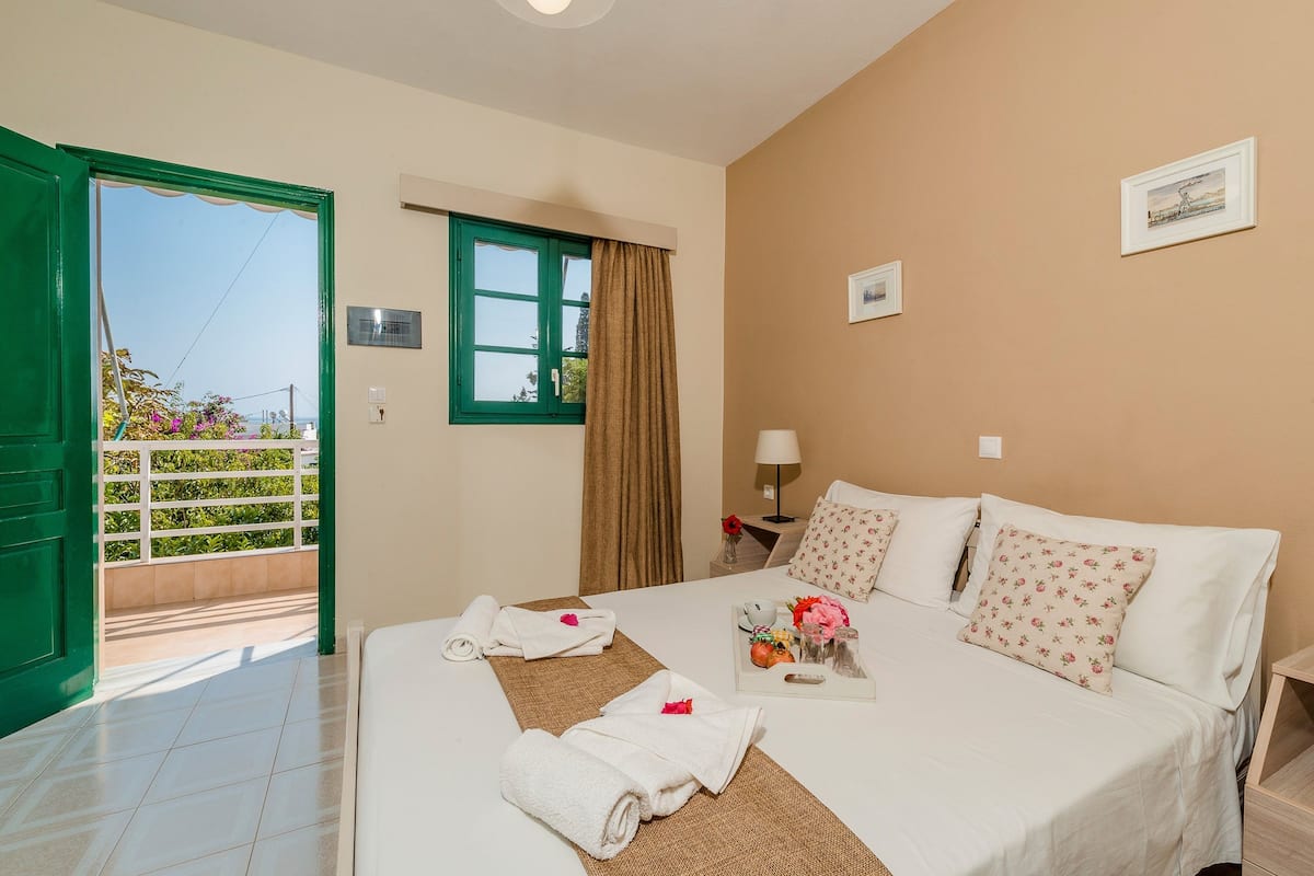 A hotel room with a bed, a nightstand, a lamp, a window with curtains, and a view of the outside.