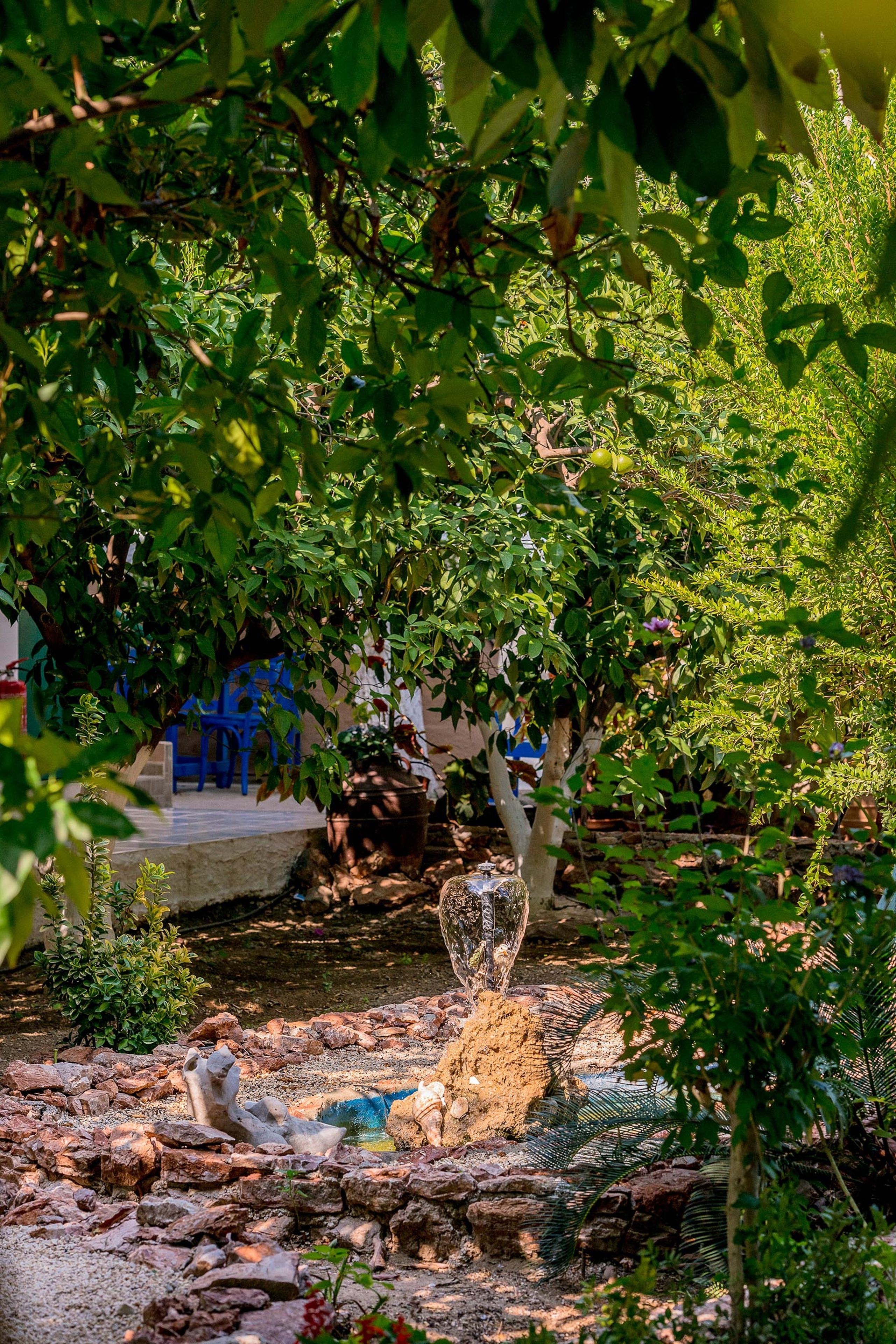 A garden with a water feature, a stone sculpture, and a blue chair.