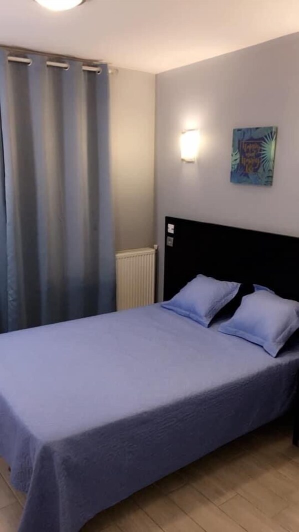 A bedroom with a bed, curtains, a wall-mounted light, and a painting. - Hôtel des Arcades (Rouen)