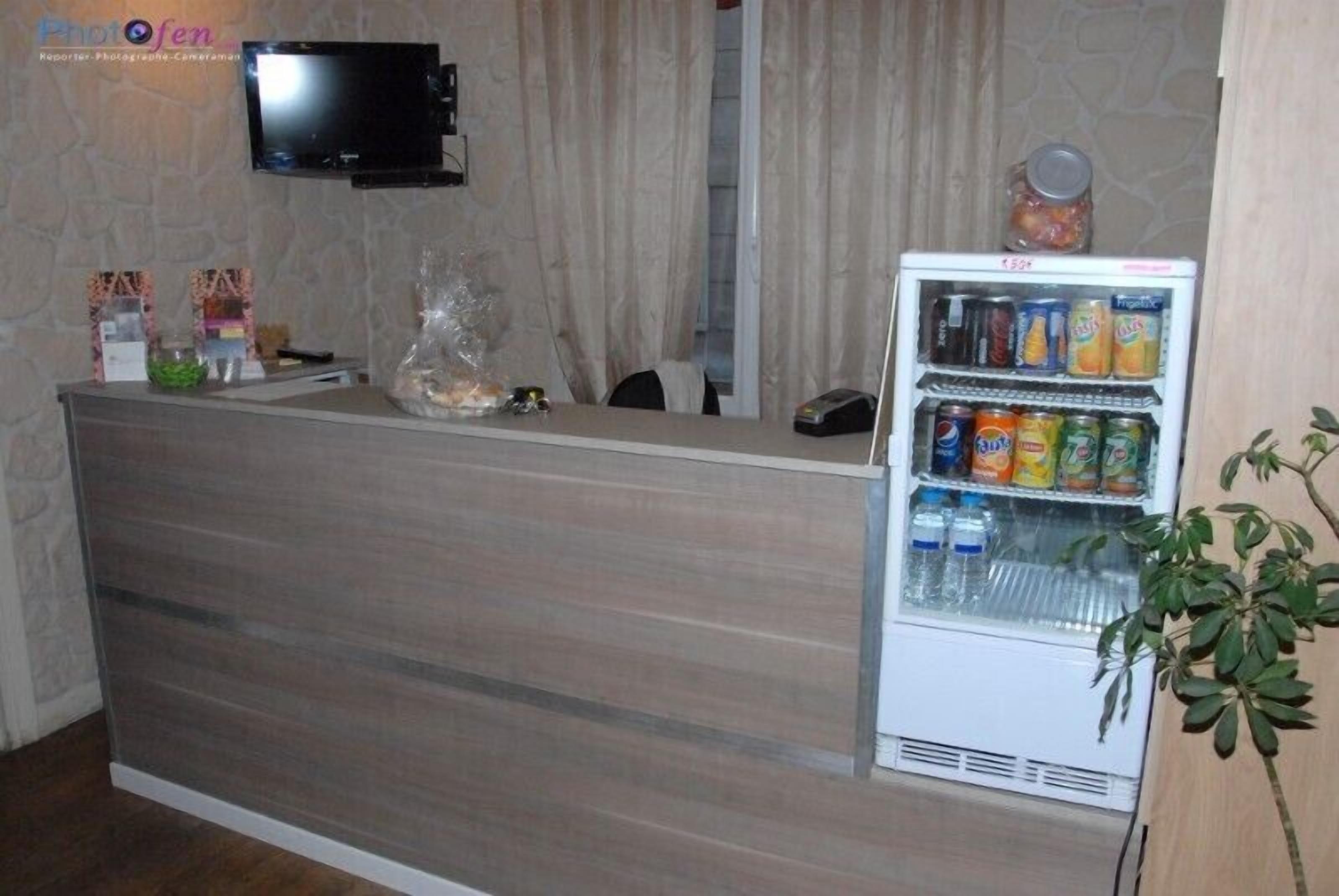 Un espace d’accueil doté d’un comptoir en bois, d’un téléviseur fixé au mur et d’un réfrigérateur rempli de boissons.
