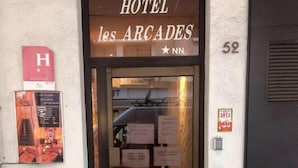A entrada do Hotel Les Arcades, com uma placa acima da porta e o número '52' na parede à direita.