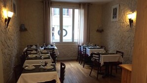 Uma sala de jantar com várias mesas postas, paredes de pedra e uma janela com cortinas.