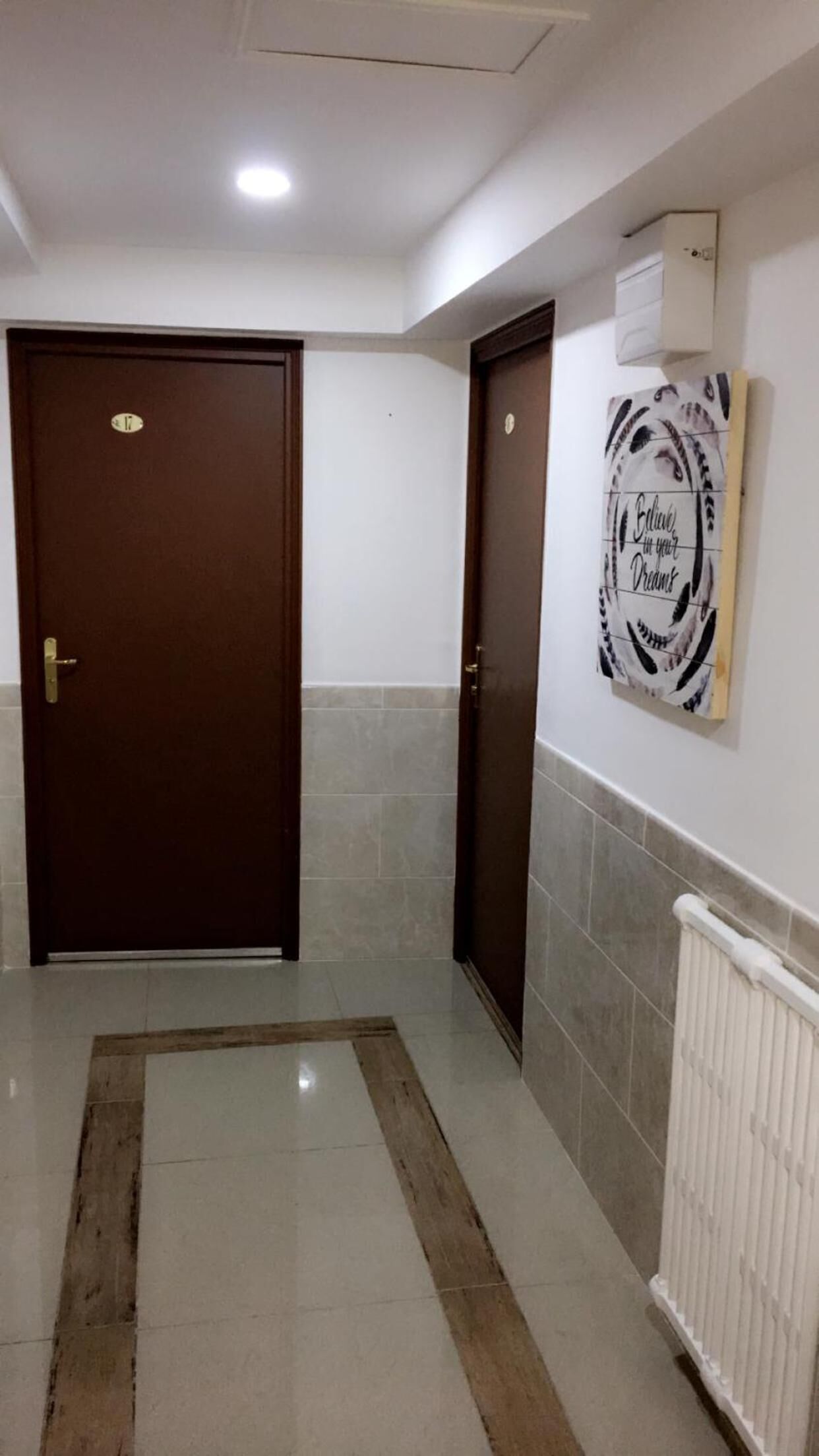 A hallway with two doors, a radiator, and a motivational quote on the wall.