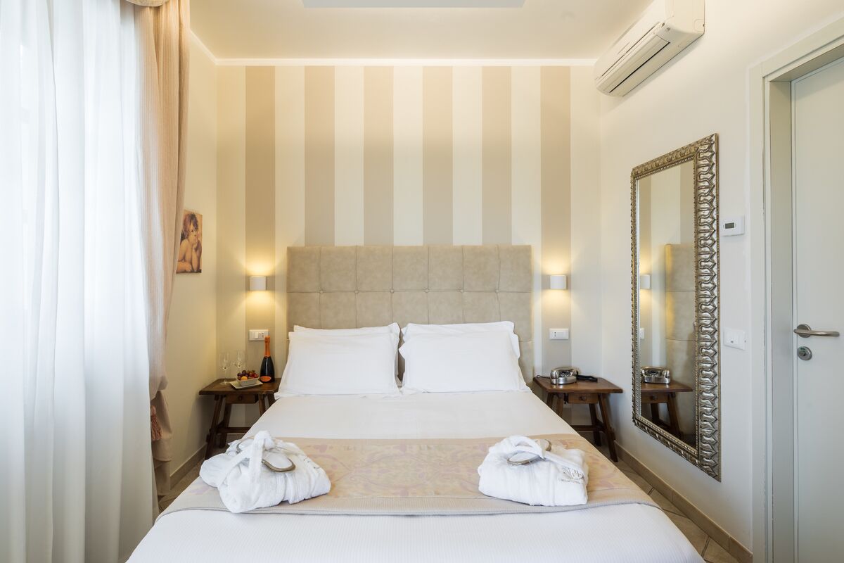 Quarto de hotel com uma cama grande, duas mesas de cabeceira, um espelho e uma porta.