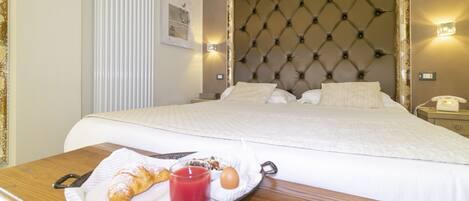 A neatly made bed with a tufted headboard, a bedside table with a tray of breakfast including a croissant, a glass of juice, and an egg.