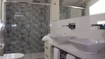 Un baño con ducha, dos lavamanos, inodoro y azulejos estampados.
