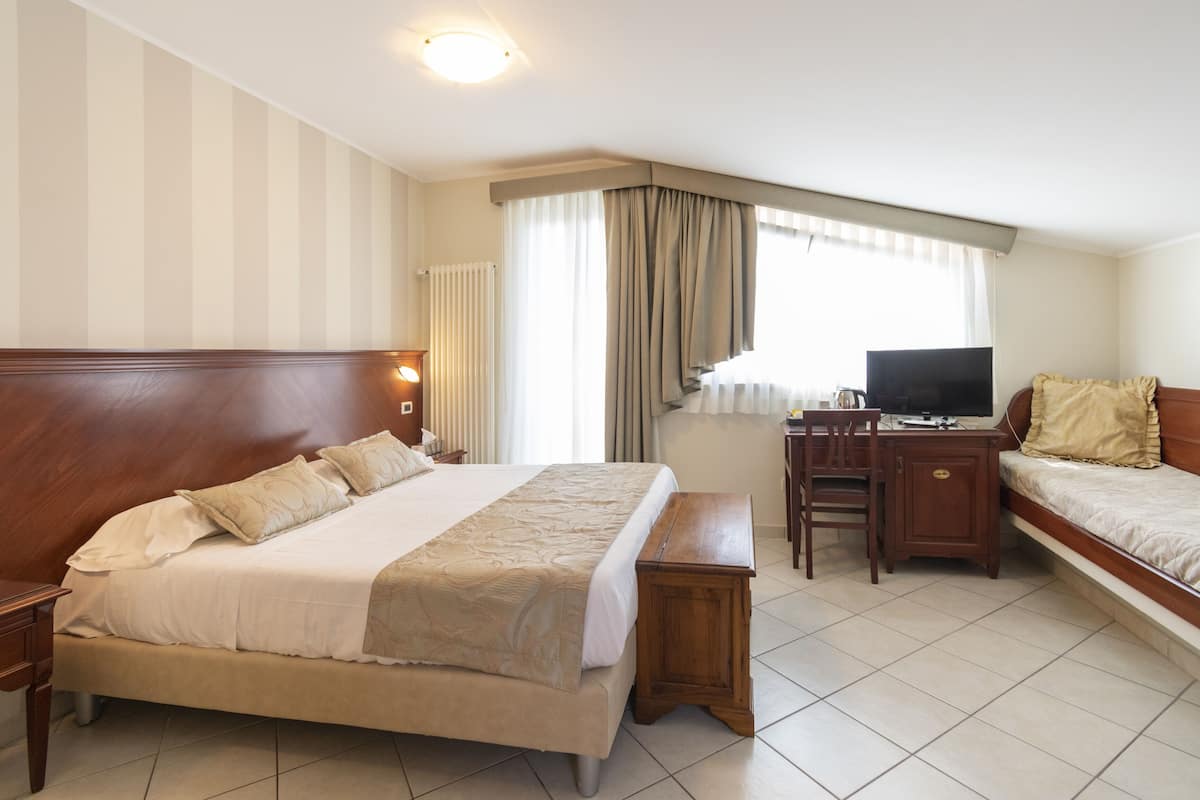 A hotel room with a large bed, a desk with a computer, a TV, and a small sofa.