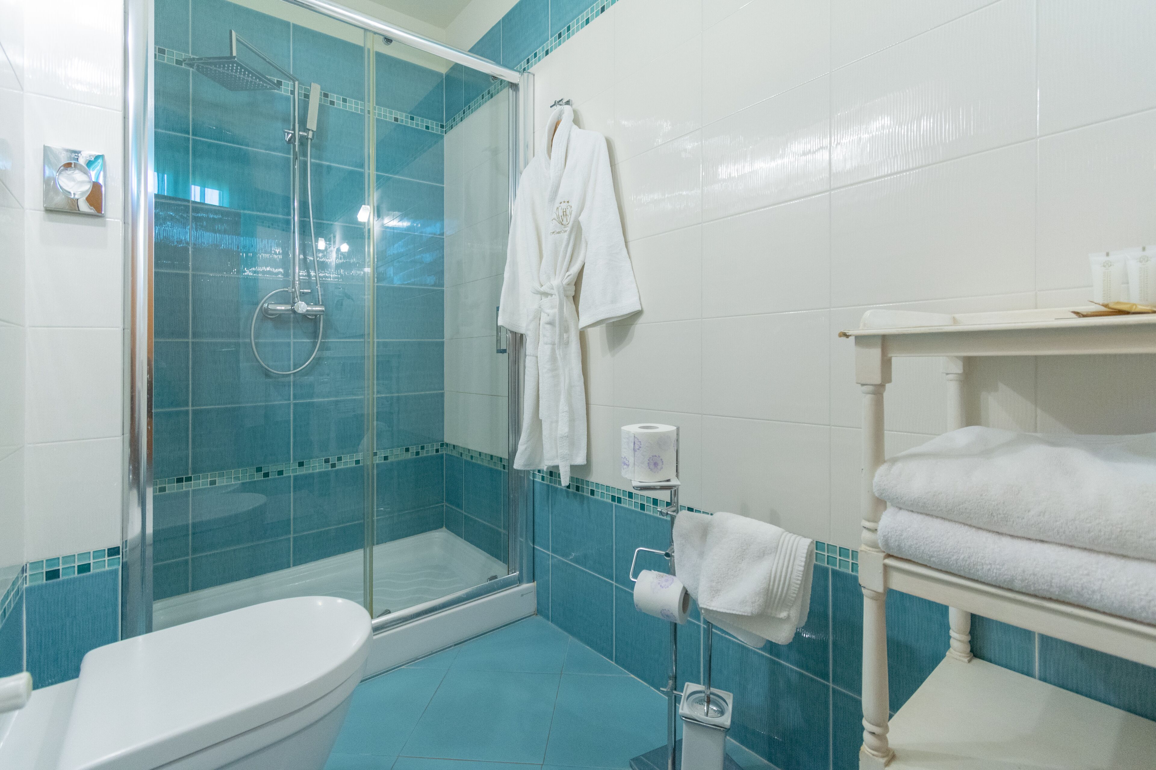 A bathroom with a glass-enclosed shower, a toilet, a sink, and a towel rack with folded towels.