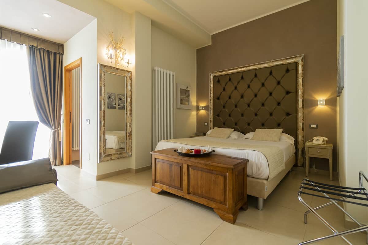 A spacious bedroom with a large bed, a wooden bedside table, a nightstand, and a chair.