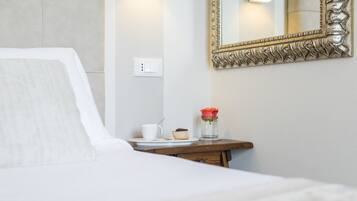 Una habitación de hotel con una cama, una mesita de noche con una taza, un muffin y un florero con una flor.