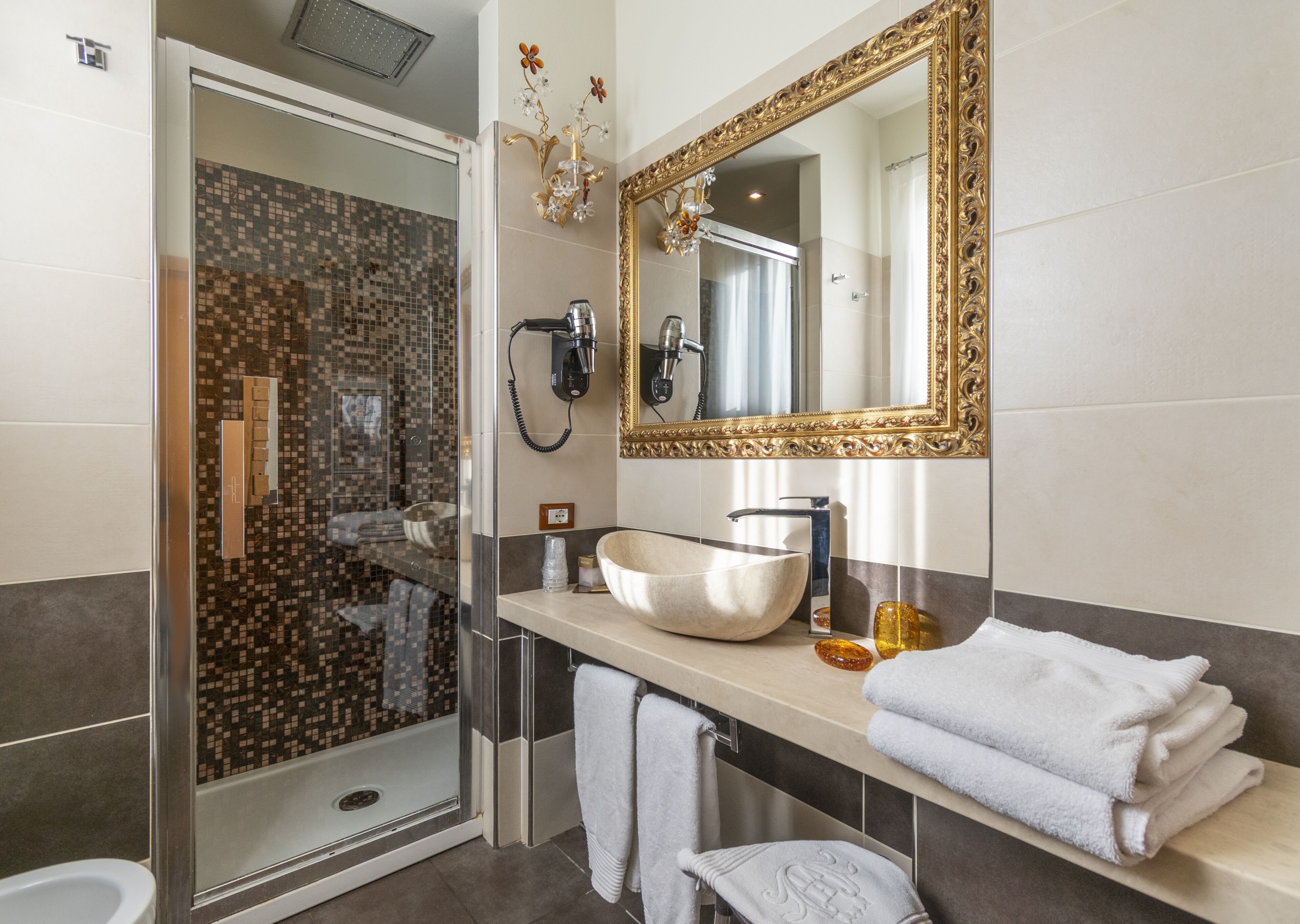 Un baño moderno con ducha de vidrio, un espejo grande, un lavamanos tipo recipiente y toallas dobladas con cuidado.